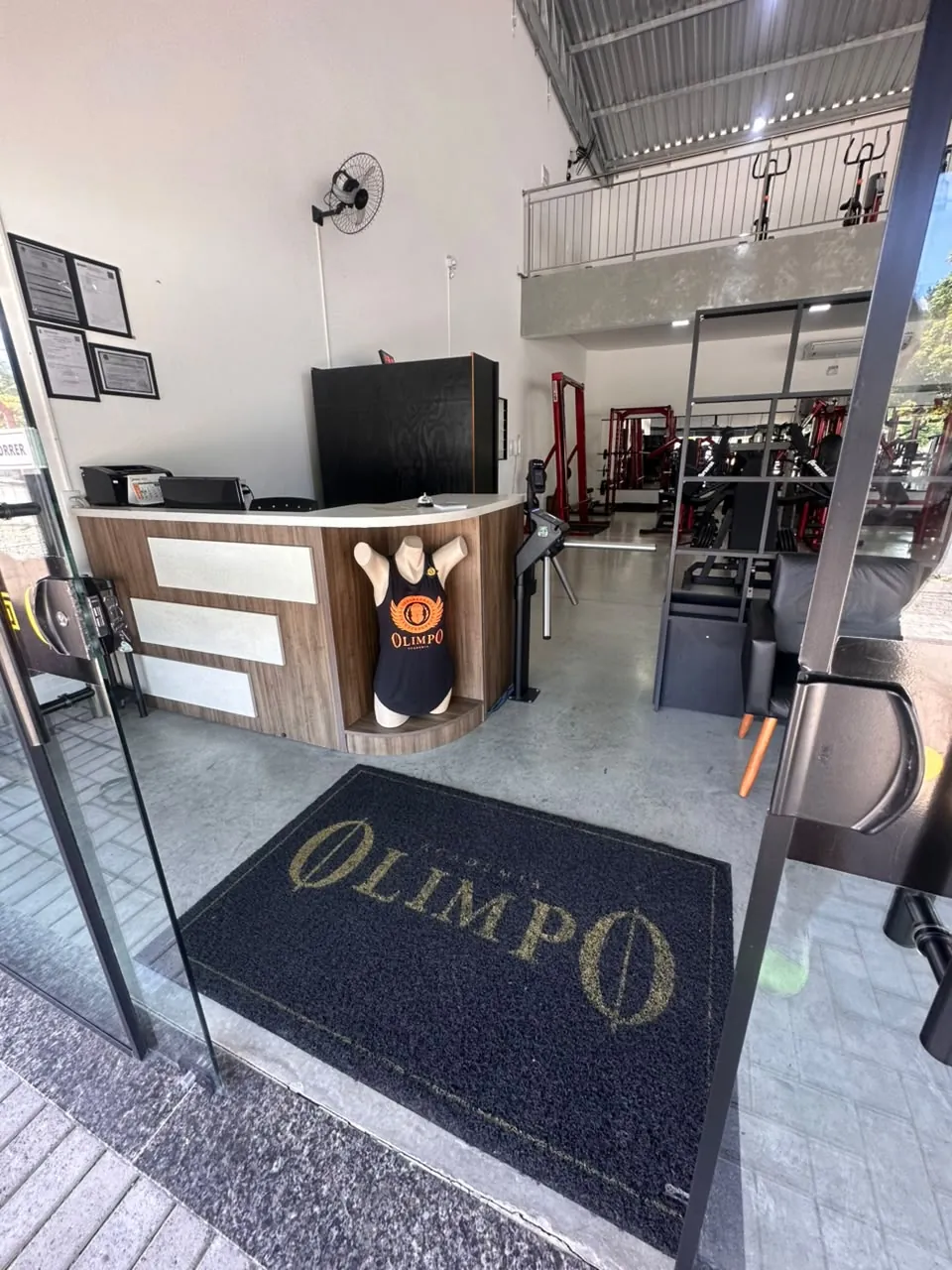 Recepção da Olimpo Atena, com balcão, catraca de acesso e tapete com a marca Olimpo